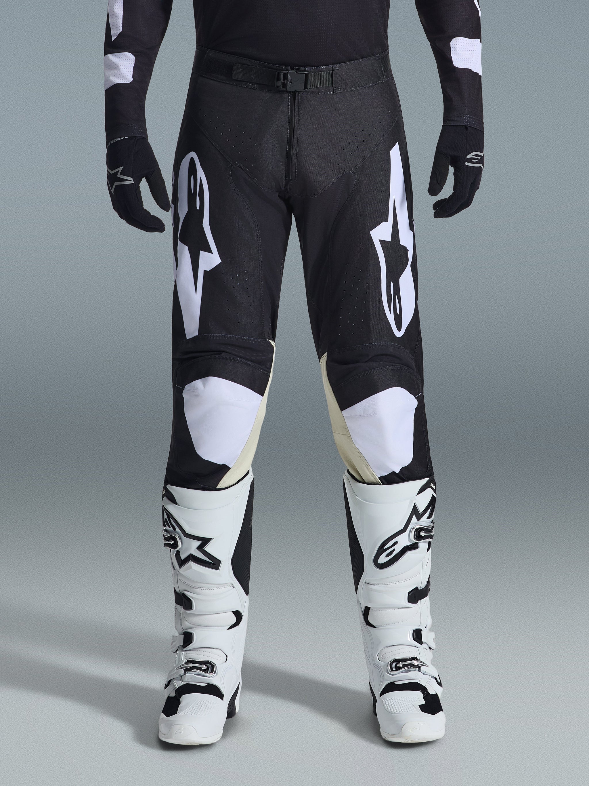 Alpinestars 2026 Racer Air Riway Pants, pantalones de motocross, negro y blanco, con llamativos logotipos blancos de Alpinestars en los muslos y paneles de las rodillas, combinados con botas de motocross blancas y negras y guantes negros, diseño atlético de ajuste de carrera para conducción off-road