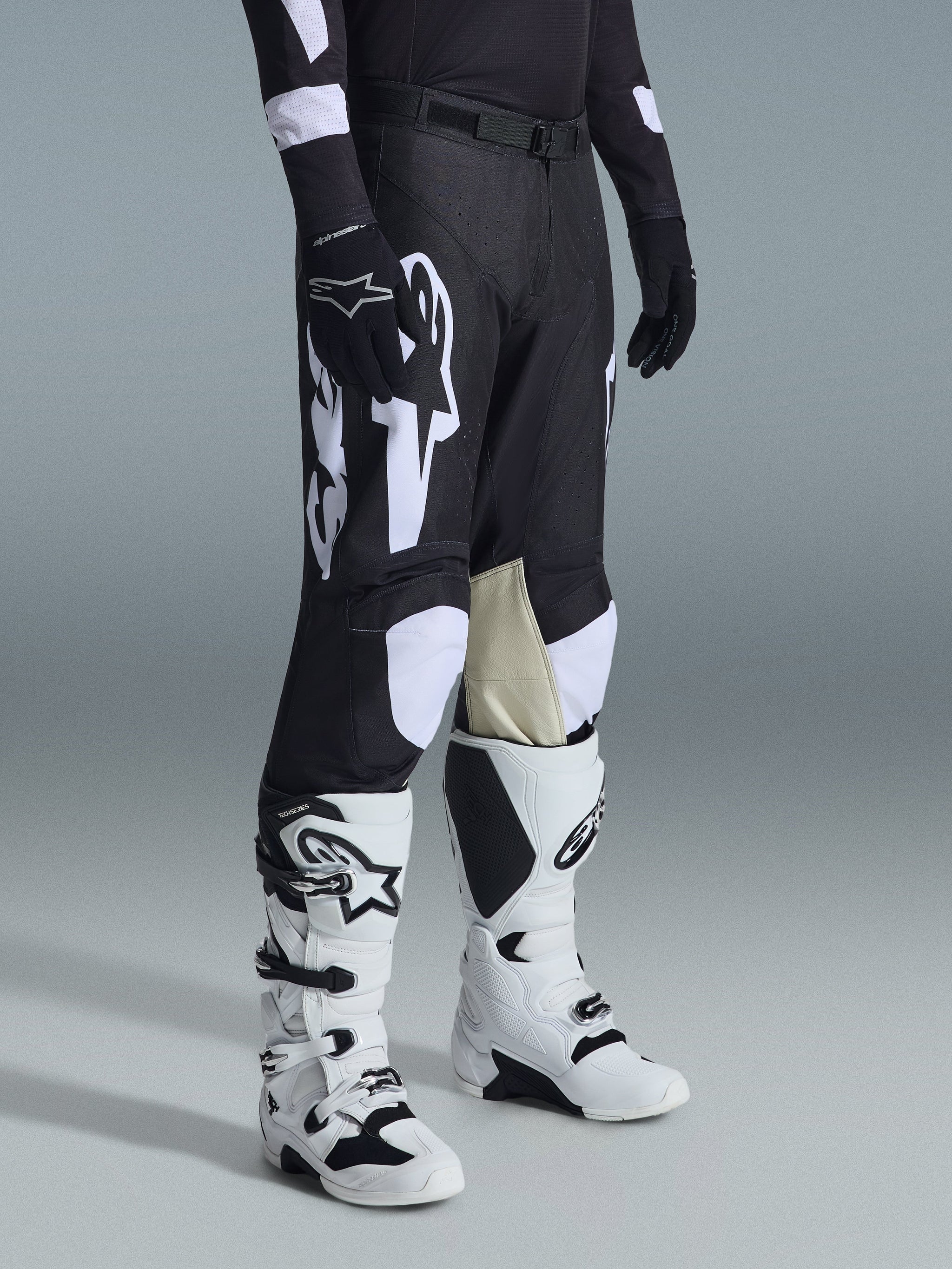 Pantalones Alpinestars Racer Air Riway 2026, pantalones de motocross negros y blancos, usados con botas Tech Series blancas y negras y jersey negro de manga larga, con logotipos Alpinestars en blanco, perforaciones cortadas con láser y paneles interiores de la rodilla en cuero de cabra color canela para rendimiento off-road.