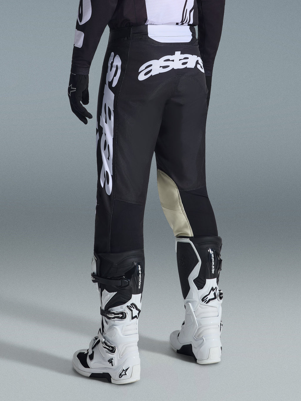 Vista trasera de los pantalones Alpinestars 2026 Racer Air Riway en negro y blanco, con el prominente logotipo 'astars' en blanco en el asiento y la pierna, paneles interiores de la rodilla en cuero crema, combinados con botas y jersey de motocross a juego en negro y blanco.