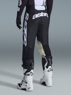 Vista trasera de los pantalones Alpinestars 2026 Racer Air Riway en negro y blanco, con el prominente logotipo 'astars' en blanco en el asiento y la pierna, paneles interiores de la rodilla en cuero crema, combinados con botas y jersey de motocross a juego en negro y blanco.