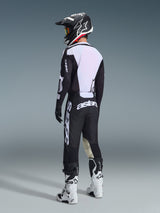 Piloto de motocross visto desde atrás vistiendo los pantalones Alpinestars 2026 Racer Air Riway en negro y blanco, combinados con un jersey ventilado a juego, casco en blanco y negro y botas de motocross blancas, con el destacado logotipo 'astars' blanco en el asiento.