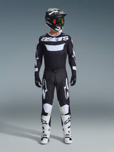 Piloto de motocross con pantalones Alpinestars Racer Air Riway 2026 en negro y blanco, jersey a juego con el logo 'astars', casco negro, gafas con lentes iridiscentes y botas de carreras blancas, conjunto completo de equipamiento profesional para off-road