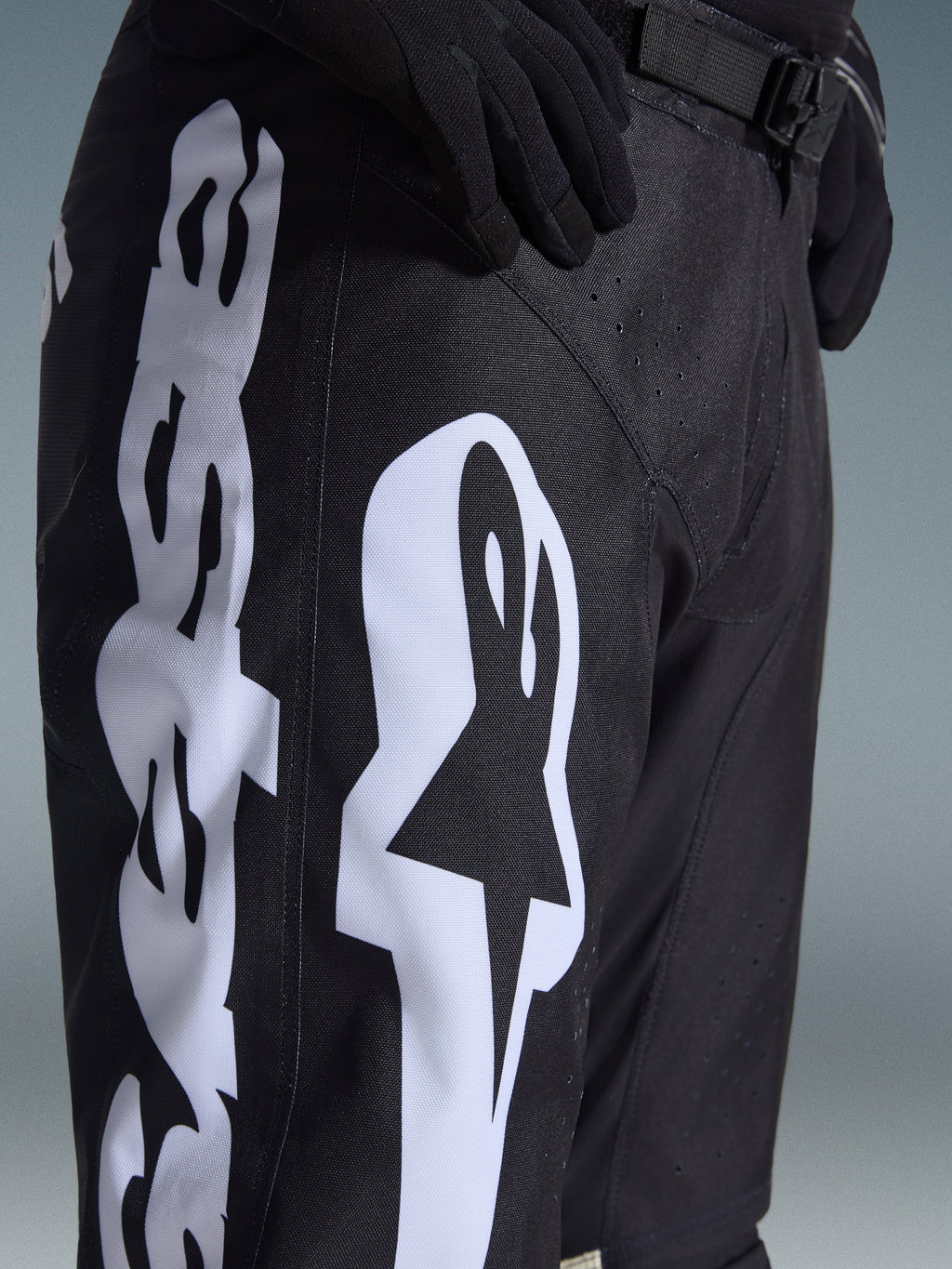 Alpinestars 2026 Racer Air Riway Pants, pantalones de motocross, blanco y negro, vista de primer plano con la marca Alpinestars en blanco, perforaciones láser para el flujo de aire y hebilla de cintura ajustable, tejido duradero para conducción off-road