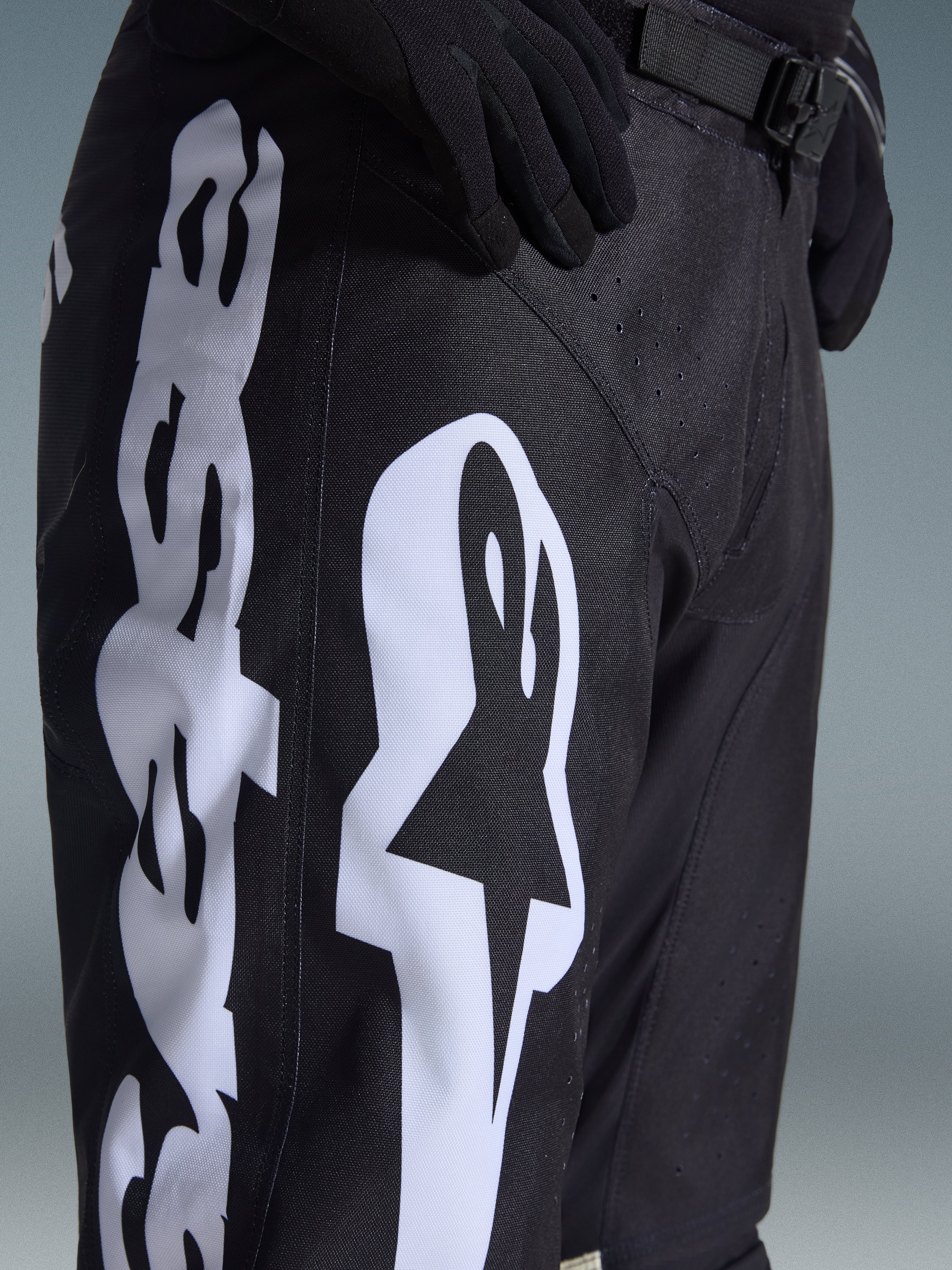 Alpinestars 2026 Racer Air Riway Pants, pantalones de motocross, blanco y negro, vista de primer plano con la marca Alpinestars en blanco, perforaciones láser para el flujo de aire y hebilla de cintura ajustable, tejido duradero para conducción off-road