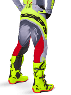 Alpinestars Techstar Melt Pants 2025, pantalones de motocross, rojo brillante y gris con detalles en amarillo neón, vista trasera que destaca el logotipo negro en el asiento, usados con botas amarillo neón y jersey gris, ajuste atlético de competición para off-road.