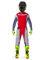 Piloto de motocross con el conjunto Alpinestars 2025 Techstar Melt en rojo brillante y gris, con jersey rojo de mangas grises, pantalones grises con acentos rojos y amarillo neón, botas y guantes amarillo neón coordinados, y casco negro con gafas amarillo neón