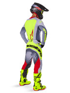 Alpinestars 2025 Techstar Melt, conjunto de equipo de motocross visto desde atrás, jersey gris con panel trasero amarillo neón y logo de estrella roja, pantalones grises y rojos con marca 'Alpinestars' en amarillo neón en la parte trasera, botas de motocross amarillo neón brillante y casco a juego