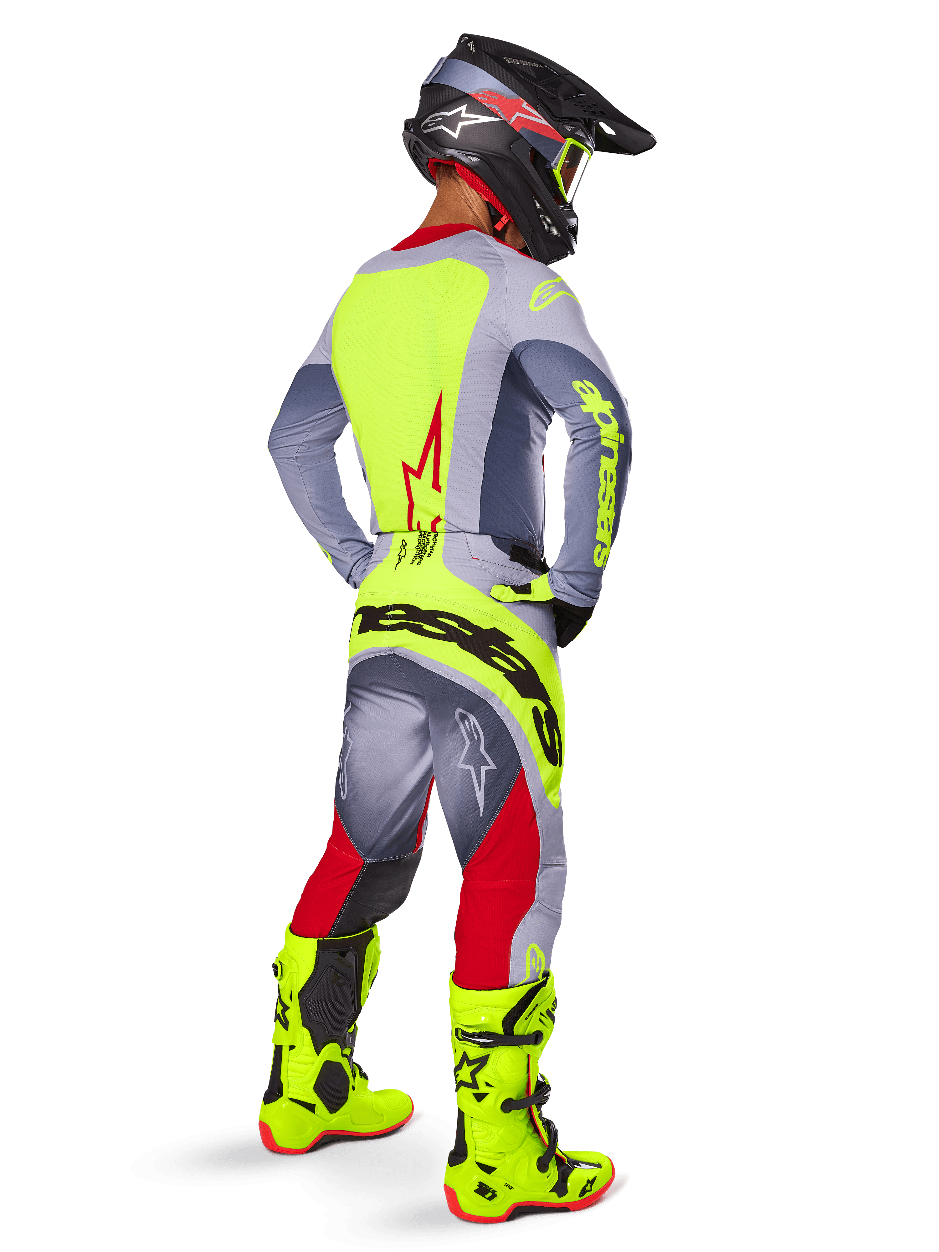 Piloto de motocross en vista de tres cuartos trasera con pantalones Alpinestars 2025 Techstar Melt en rojo brillante y gris, llamativo logotipo amarillo neón en la parte trasera, jersey a juego en gris y amarillo neón, botas amarillo neón brillante y casco negro con gafas neón, conjunto de equipamiento profesional para carreras todoterreno.