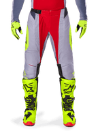Alpinestars 2025 Techstar Melt Pants, pantalones de motocross, rojo brillante y gris con detalles en amarillo fluorescente, usados con guantes y botas amarillo neón a juego, con hebilla magnética en la cintura y perforaciones láser para ventilación.