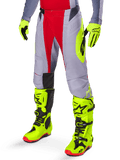 Alpinestars Techstar Melt Pants 2025, pantalones de motocross en rojo brillante y gris, con gráficos laterales en amarillo neón y paneles negros en las rodillas, combinados con botas y guantes amarillo neón a juego, diseñados para un rendimiento competitivo off-road