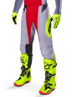 Alpinestars Techstar Melt Pants 2025, pantalones de motocross en rojo brillante y gris, con gráficos laterales en amarillo neón y paneles negros en las rodillas, combinados con botas y guantes amarillo neón a juego, diseñados para un rendimiento competitivo off-road