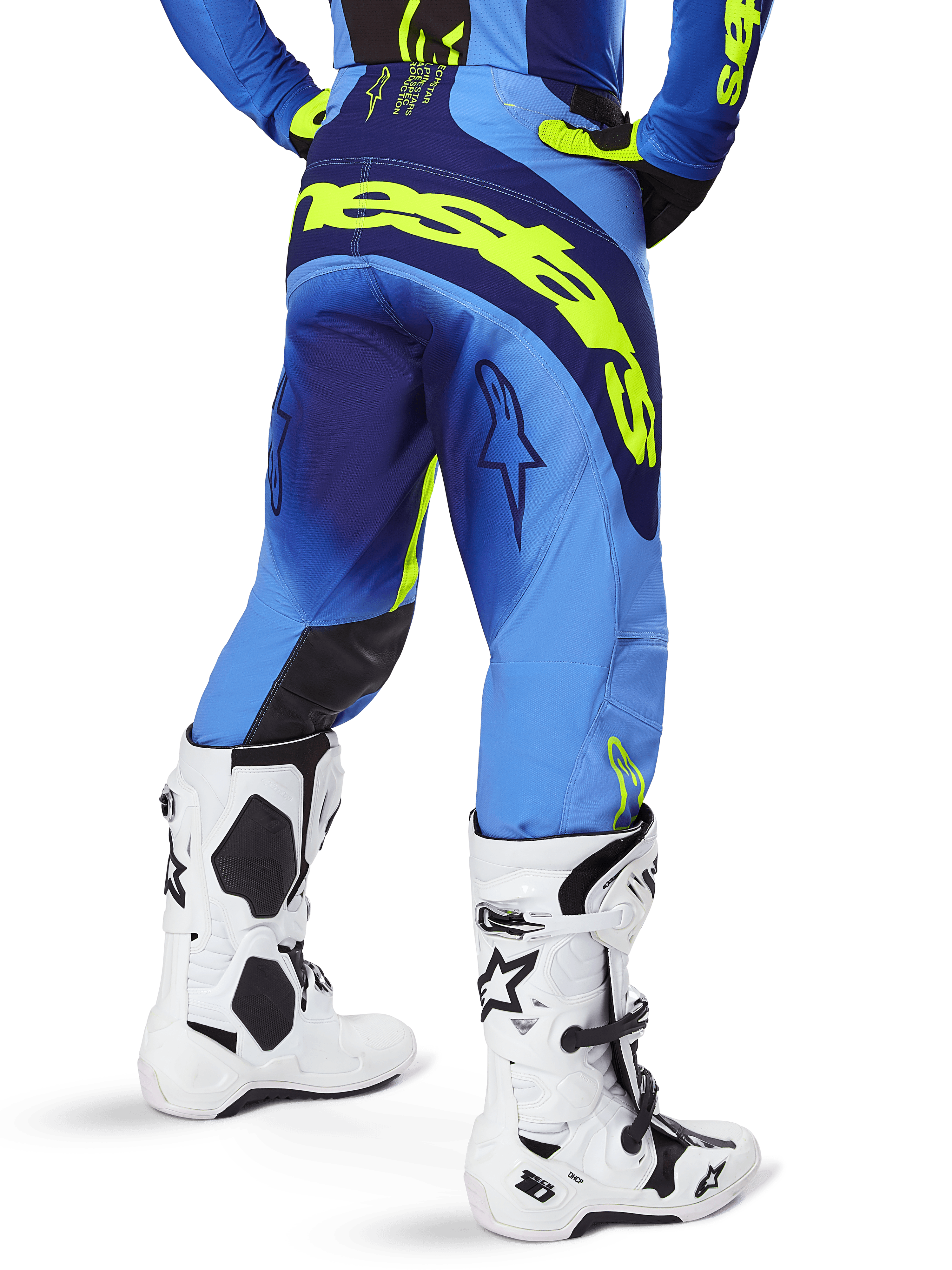 Pantalones Alpinestars Techstar Melt 2025, pantalones de motocross, azul y amarillo flúor, vista trasera que muestra un gran logotipo amarillo en el asiento y los muslos, usados con botas de motocross blancas y jersey azul a juego, ajuste atlético de competición para conducción off-road