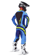 Pantalones Alpinestars 2025 Techstar Melt, equipamiento de motocross, amarillo flúor y azul, vista trasera de un piloto con jersey azul a juego y grandes logotipos amarillos, botas blancas y negras, y casco negro, conjunto de carreras coordinado para rendimiento todoterreno