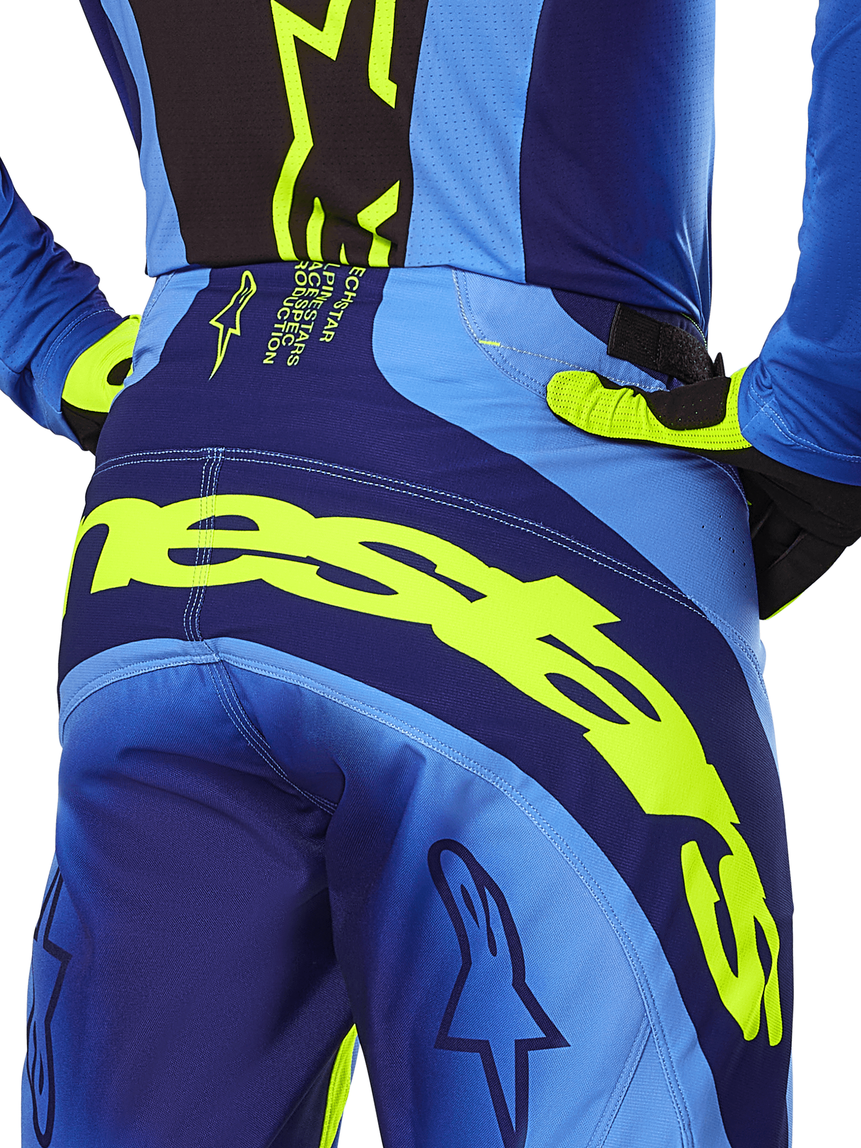 Alpinestars Techstar Melt Pants 2025, pantalones de motocross, amarillo flúor y azul, primer plano de la vista trasera con la marca Alpinestars en amarillo llamativo en la zona del asiento, combinados con jersey azul y guantes amarillo flúor, diseñados para competición off-road de alto rendimiento