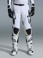 Alpinestars 2026 Racer Riway Pants, pantalones de motocross, blanco y negro, combinados con botas de motocross blancas y negras a juego y guantes negros, con el logotipo de Alpinestars en negro en los muslos, diseño técnico para rendimiento off-road.