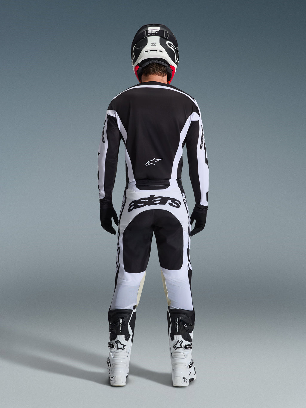 Pantalones Alpinestars 2026 Racer Riway, pantalones de motocross, blanco y negro, vista posterior del conjunto completo de equipamiento de competición, marca 'astars' llamativa en la zona del asiento, usados con jersey a juego, botas blancas y casco negro, atuendo coordinado de carreras off-road.