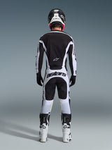 Pantalones Alpinestars 2026 Racer Riway, pantalones de motocross, blanco y negro, vista posterior del conjunto completo de equipamiento de competición, marca 'astars' llamativa en la zona del asiento, usados con jersey a juego, botas blancas y casco negro, atuendo coordinado de carreras off-road.