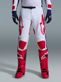 Alpinestars 2026 Racer Riway Pants, pantalones de motocross, blanco, azul y rojo, usados con botas rojas y guantes azul marino, con grandes logotipos rojos en los muslos y paneles rojos en las rodillas, diseño deportivo precurvado con hebilla de cintura ajustable