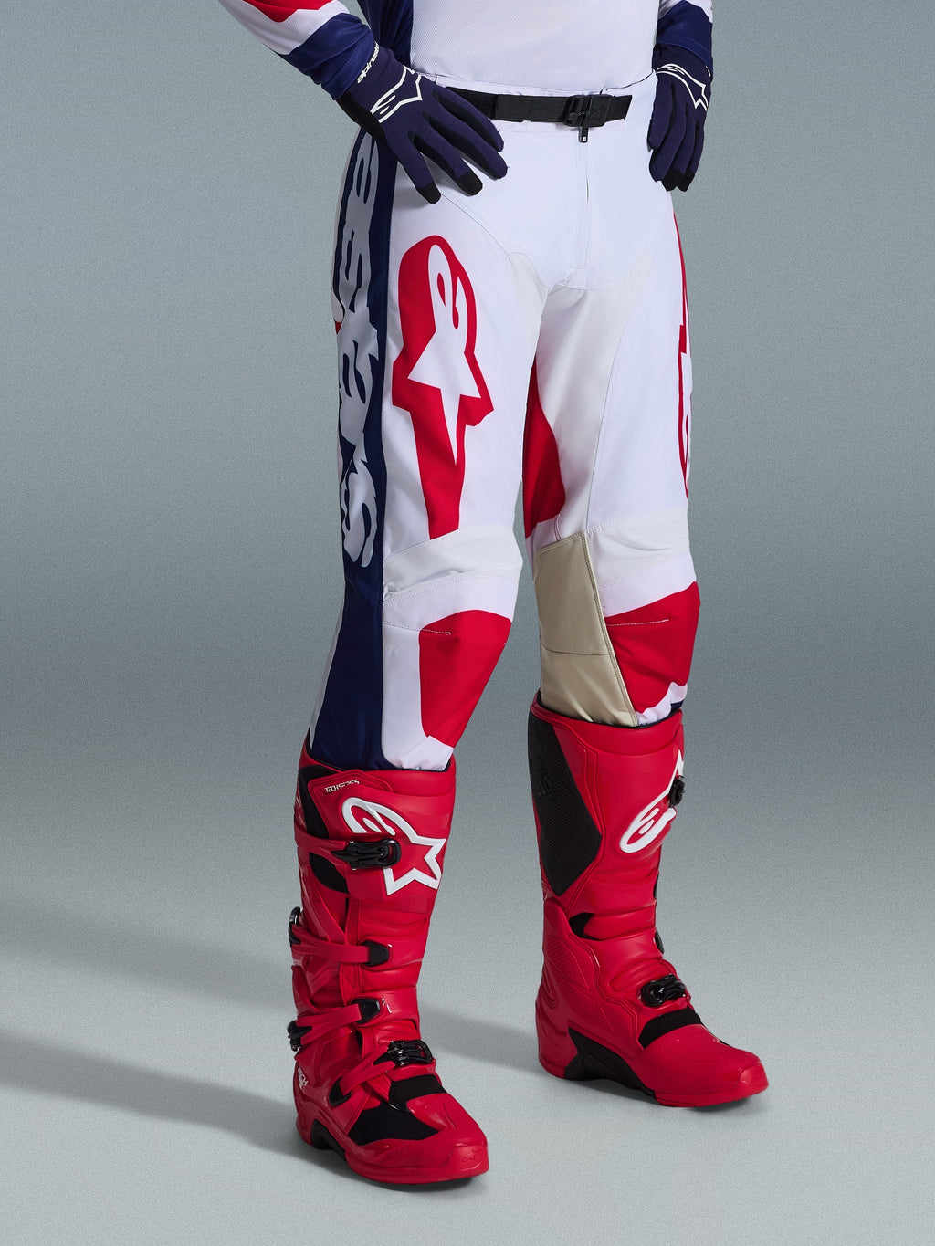 Pantalones Alpinestars Racer Riway 2026, pantalones de motocross, blanco, azul y rojo, con logotipos rojos llamativos en los muslos y paneles laterales azules con marca blanca, usados con botas rojas y guantes azul oscuro, diseño ergonómico para carreras off-road