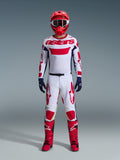 Piloto de motocross con el conjunto Alpinestars 2026 Racer Riway, jersey blanco con marca "astars" roja y paneles laterales azules, pantalones blancos con gráficos rojos, casco y botas de carreras rojas, guantes azul marino, equipamiento completo y coordinado para carreras de motocross