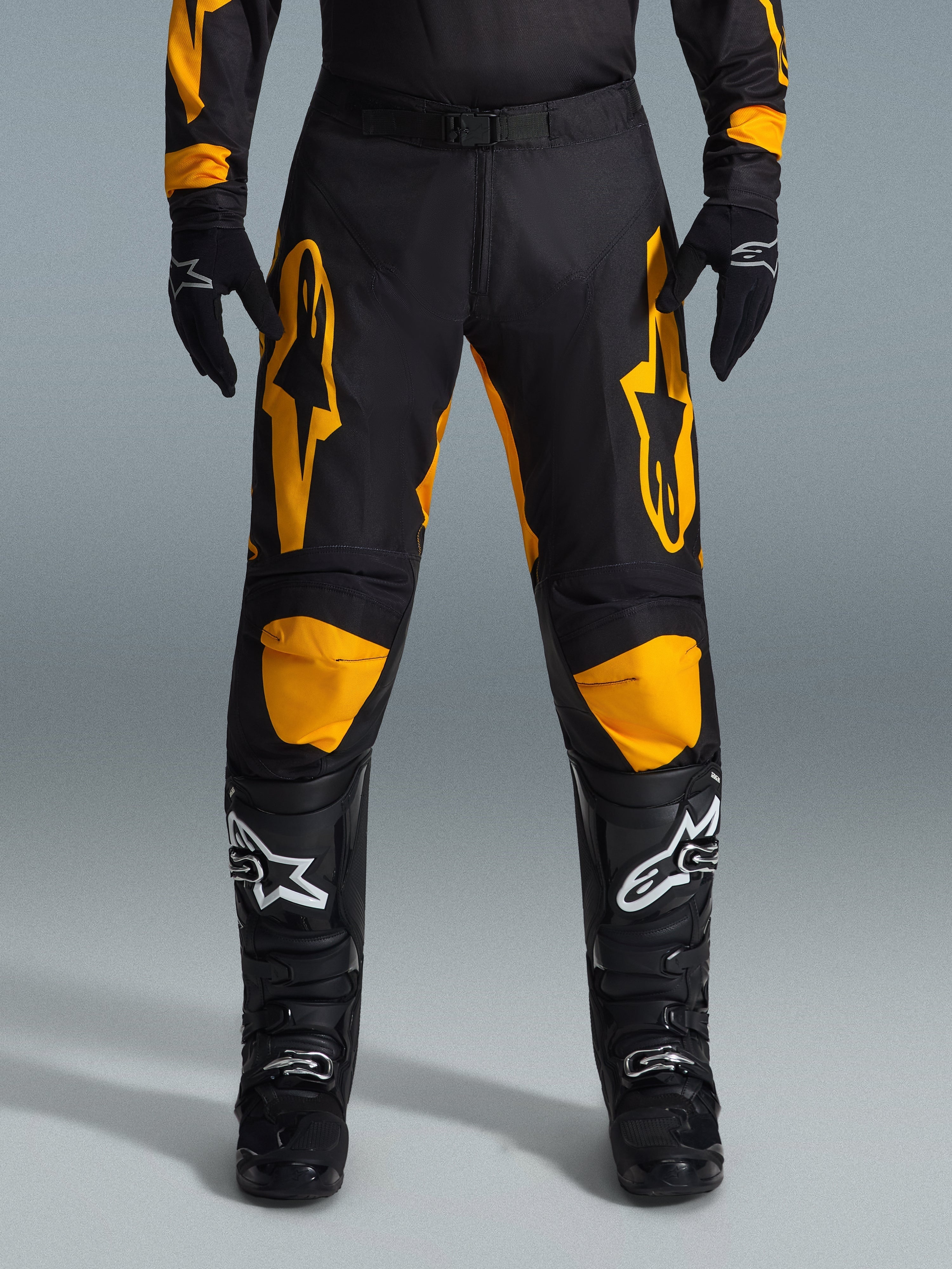 Alpinestars 2026 Racer Riway Pants, Motocross Pants, Yellow and Black, worn with black motocross gloves and black boots with white logos, featuring large yellow Alpinestars logos on the thighs and yellow knee panels, durable design for off-road racing performance