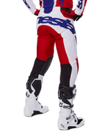 Alpinestars 2025 Racer Veil Pants, pantalones de motocross, rojo brillante y blanco con detalles de marca en azul, vista trasera que muestra los paneles de ventilación elásticos negros en la parte posterior de las piernas, combinados con botas de motocross blancas.