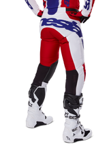 Alpinestars 2025 Racer Veil Pants, pantalones de motocross, rojo brillante y blanco con detalles de marca en azul, vista trasera que muestra los paneles de ventilación elásticos negros en la parte posterior de las piernas, combinados con botas de motocross blancas.