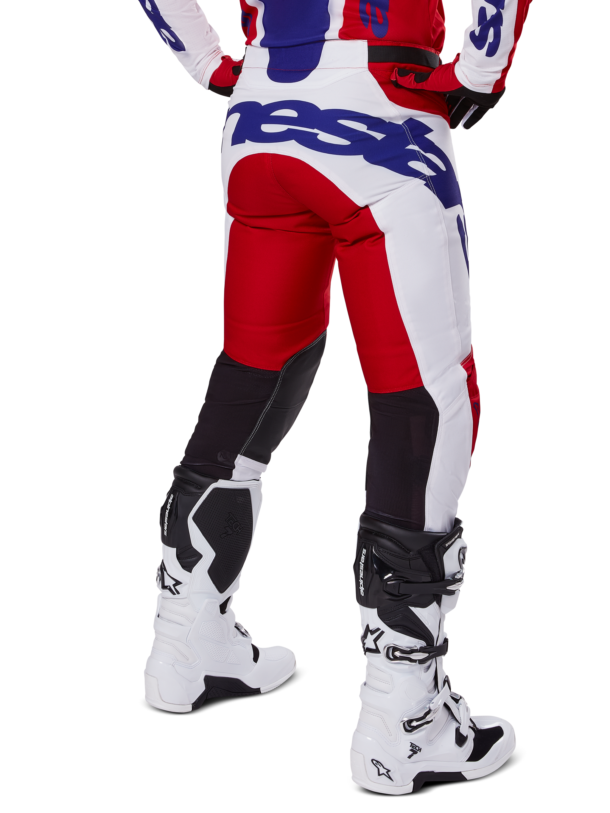 Alpinestars 2025 Racer Veil Pants, pantalones de motocross, rojo brillante y blanco con detalles de marca en azul, vista trasera que muestra los paneles de ventilación elásticos negros en la parte posterior de las piernas, combinados con botas de motocross blancas.