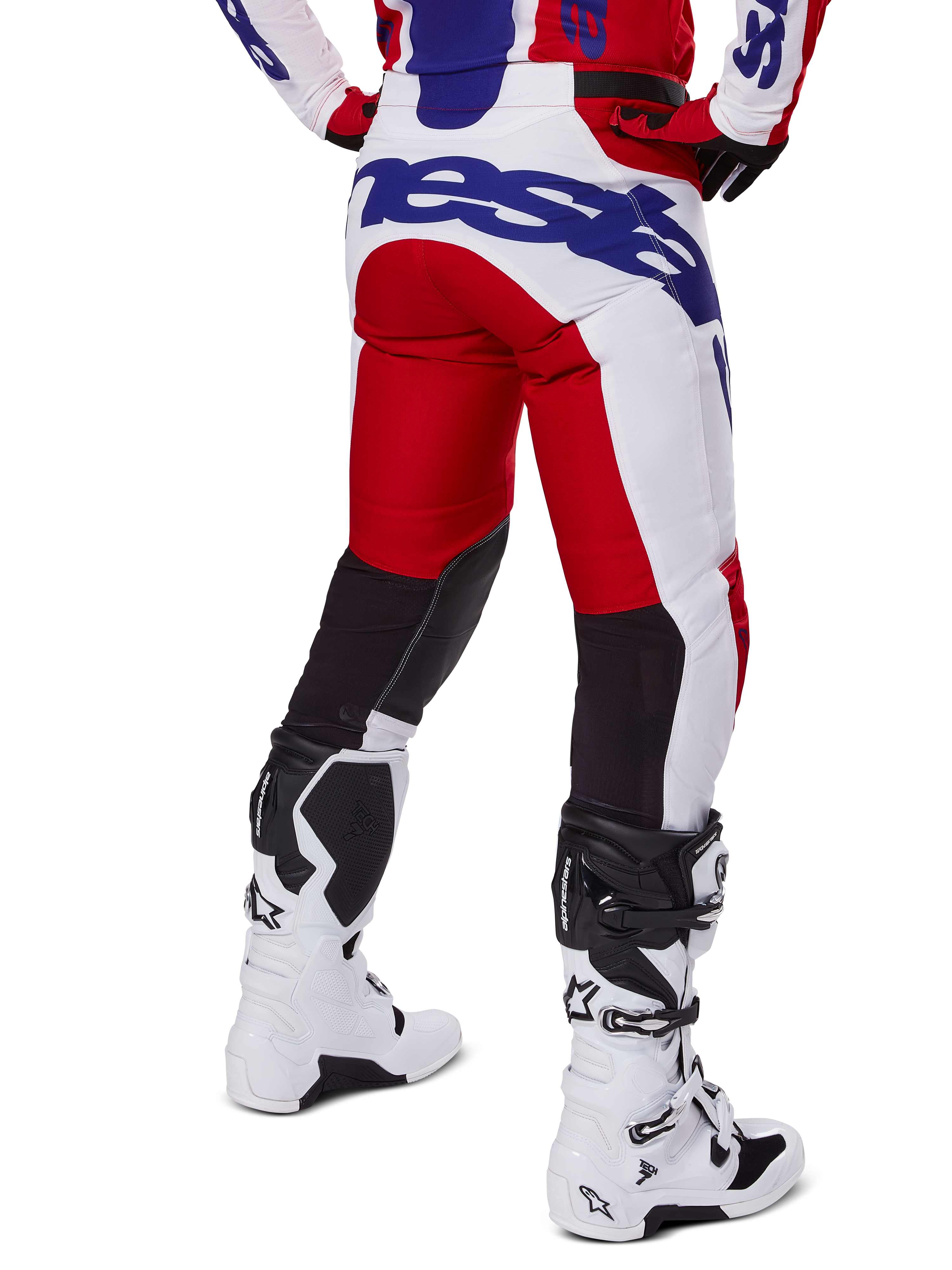 Alpinestars 2025 Racer Veil Pants, pantalones de motocross, rojo brillante y blanco con detalles de marca en azul, vista trasera que muestra los paneles de ventilación elásticos negros en la parte posterior de las piernas, combinados con botas de motocross blancas.