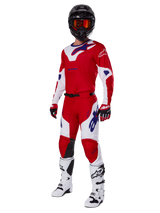 Alpinestars 2025 Racer Veil Pants, pantalones de motocross, rojo brillante y blanco, usados como parte de un conjunto completo de equipamiento de competición que incluye una camiseta roja y blanca a juego, casco negro con gafas naranjas, botas blancas y guantes rojos, con logotipos de Alpinestars en un llamativo color azul.
