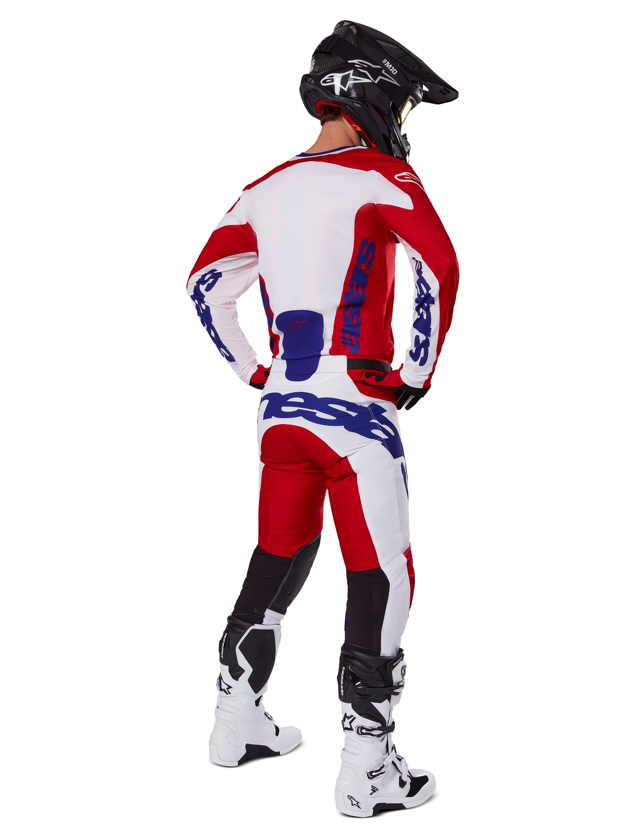 Alpinestars 2025 Racer Veil Pants, pantalones de motocross, rojo brillante y blanco con detalles azules, vistos desde atrás en un piloto con equipamiento completo, con logotipo distintivo de Alpinestars, paneles transpirables en la parte inferior de las piernas, y botas blancas y casco negro coordinados.
