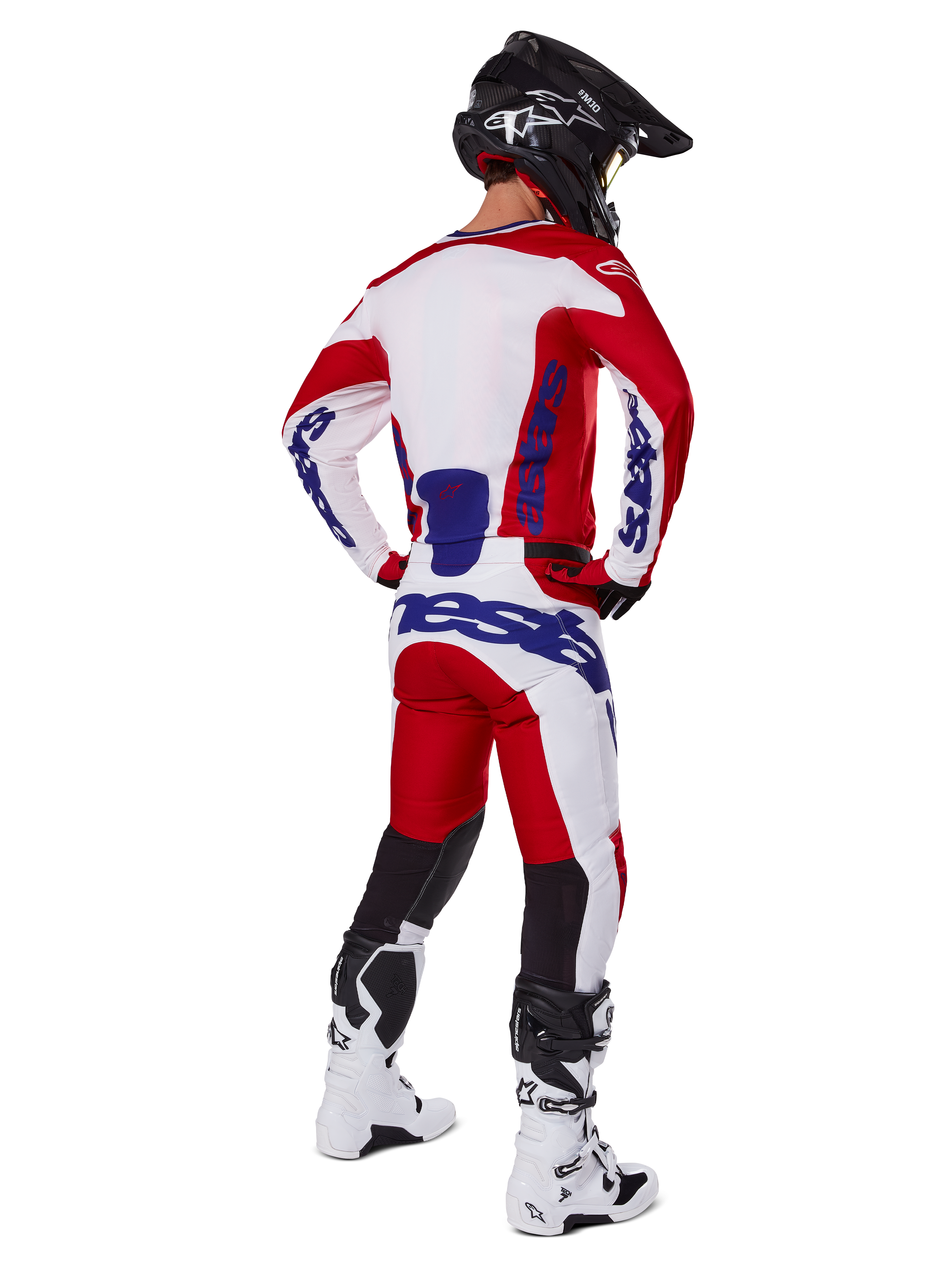 Alpinestars 2025 Racer Veil Pants, pantalones de motocross, rojo brillante y blanco con detalles azules, vistos desde atrás en un piloto con equipamiento completo, con logotipo distintivo de Alpinestars, paneles transpirables en la parte inferior de las piernas, y botas blancas y casco negro coordinados.