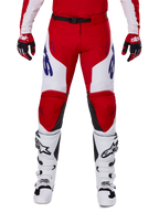 Alpinestars 2025 Racer Veil Pants, pantalones de motocross, rojo brillante y blanco, usados con guantes rojos a juego y botas blancas, con logotipos azules en los muslos y un cinturón negro, corte deportivo ergonómico para una conducción de alto rendimiento