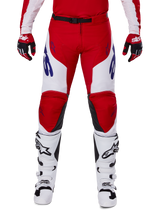 Alpinestars 2025 Racer Veil Pants, pantalones de motocross, rojo brillante y blanco, usados con guantes rojos a juego y botas blancas, con logotipos azules en los muslos y un cinturón negro, corte deportivo ergonómico para una conducción de alto rendimiento