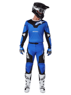 Alpinestars 2025 Racer Veil Pants, pantalones de motocross, azul y negro, usados como un conjunto de carreras completo con jersey azul y negro a juego, casco negro y blanco, guantes azules y botas blancas, con logotipos llamativos y un diseño ergonómico para conducción off-road.