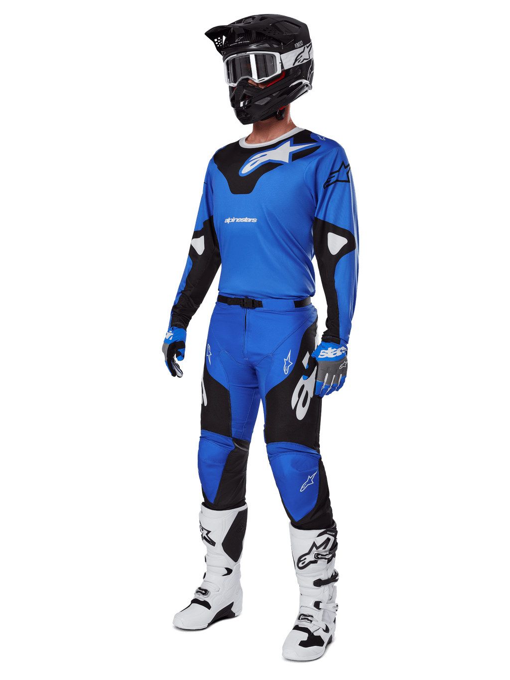 Piloto de motocross con equipamiento completo de competición, que incluye los pantalones Alpinestars 2025 Racer Veil en azul y negro, jersey azul a juego con detalles blancos, casco negro con gafas blancas, botas blancas y negras, y guantes azules, conjunto coordinado para carreras off-road