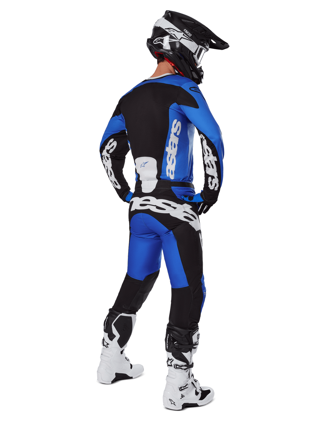 Piloto de motocross visto desde atrás con pantalones Alpinestars 2025 Racer Veil en azul y negro, jersey de manga larga a juego con logotipos blancos, botas Tech 7 en blanco y negro y casco SM10 negro, conjunto de equipamiento completo para carreras off-road