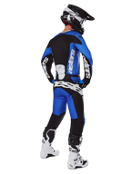 Piloto de motocross visto desde atrás con pantalones Alpinestars 2025 Racer Veil en azul y negro, jersey de manga larga a juego con logotipos blancos, botas Tech 7 en blanco y negro y casco SM10 negro, conjunto de equipamiento completo para carreras off-road