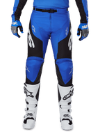 Alpinestars 2025 Racer Veil Pants, pantalones de motocross, azul y negro, con logotipos blancos de Alpinestars en las piernas y paneles laterales negros, usados con botas de motocross blancas y guantes azules y grises, equipamiento de alto rendimiento para conducción off-road