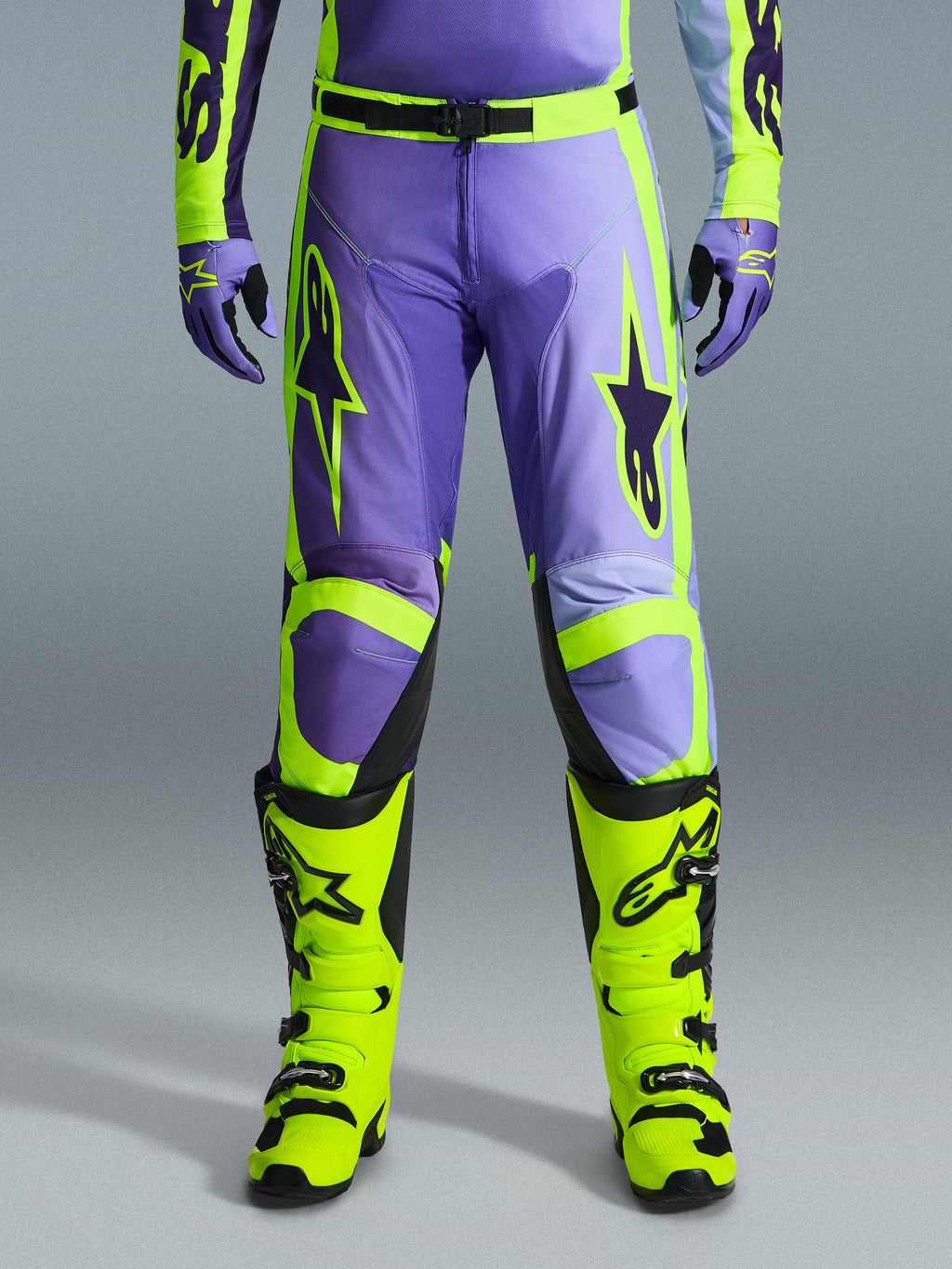 Alpinestars 2026 Racer Portl Pants, pantalones de motocross, morado y amarillo flúor, usados con botas amarillo flúor a juego y guantes morados, con grandes logotipos de estrellas y confección en poliéster duradero para carreras off-road