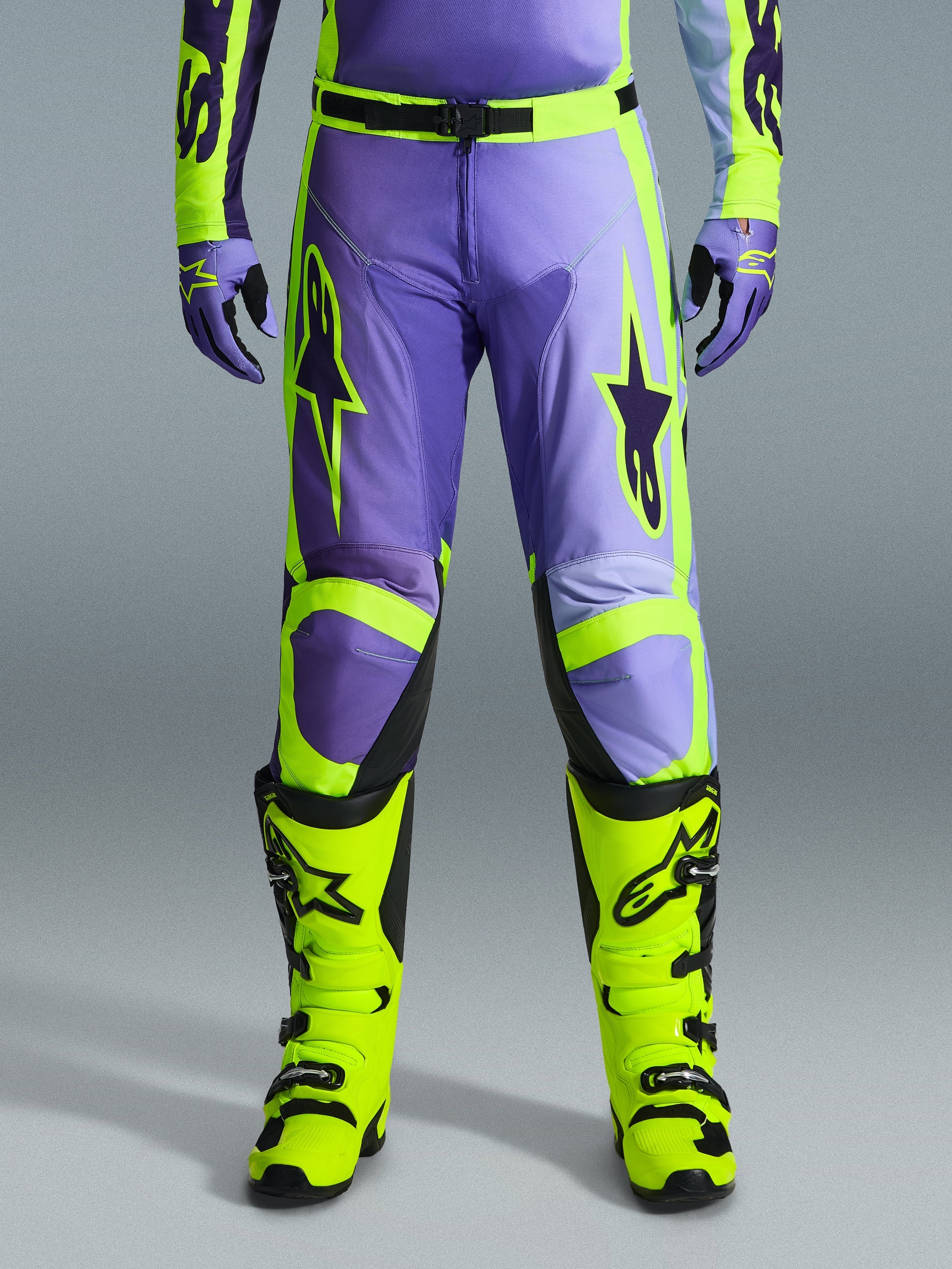 Alpinestars 2026 Racer Portl Pants, pantalones de motocross, morado y amarillo flúor, usados con botas amarillo flúor a juego y guantes morados, con grandes logotipos de estrellas y confección en poliéster duradero para carreras off-road