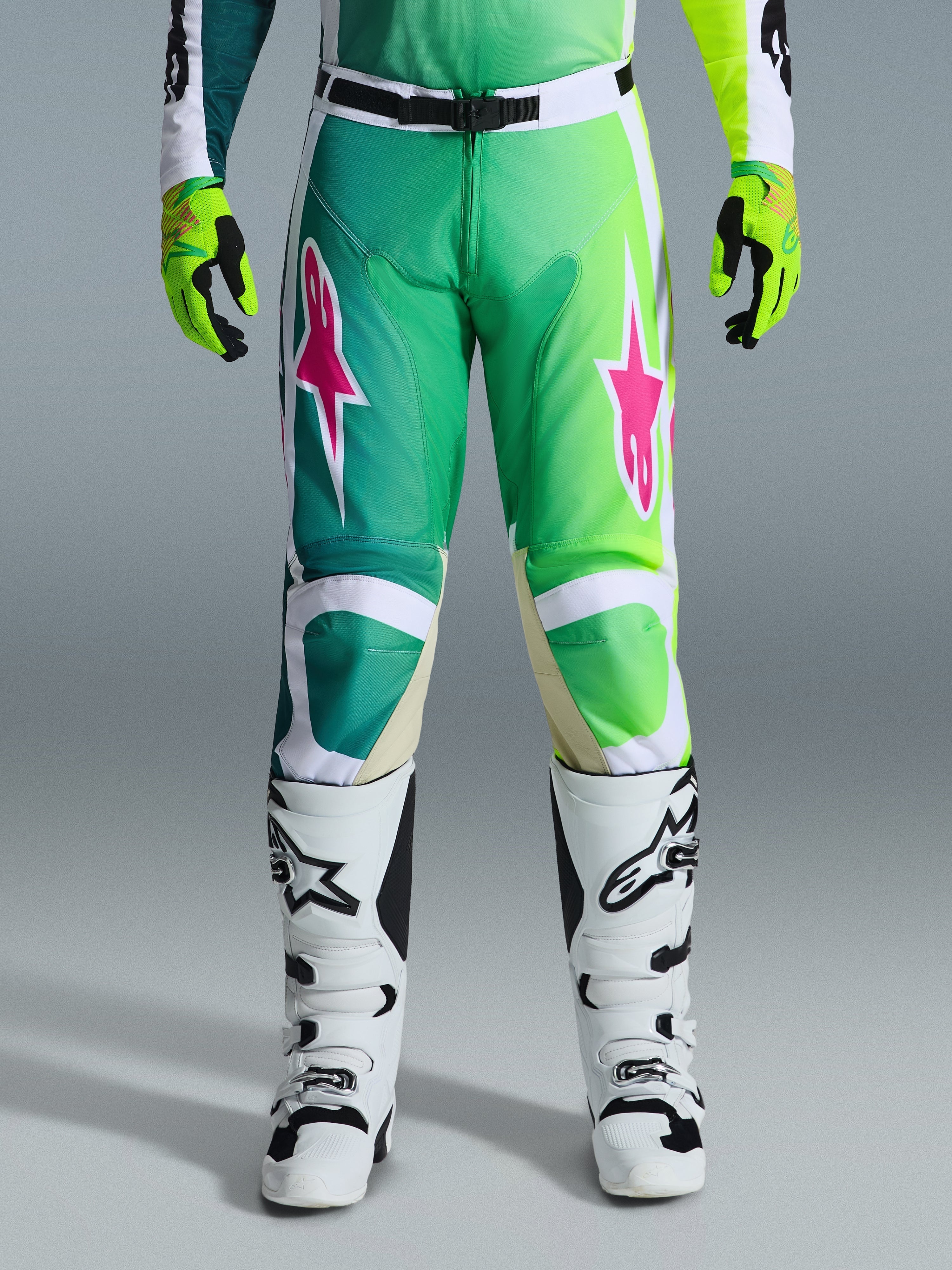 Alpinestars 2026 Racer Portl Pants, pantalones de motocross, verde, blanco y negro con logos de estrellas rosas, usados con botas blancas y negras y guantes verde lima, con un diseño en degradado y ajuste ergonómico para carreras todoterreno
