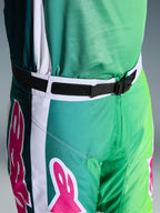 Alpinestars 2026 Racer Portl Pants, pantalones de motocross, verdes, blancos y negros con acentos del logo en rosa, primer plano de la cintura que muestra la hebilla magnética SX2 y el cierre ajustable, equipamiento duradero para carreras off-road