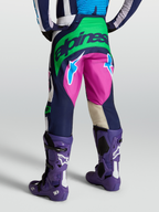 Alpinestars Techstar Maven, pantalones de motocross para hombre, azul y verde con detalles en rosa, vista trasera con botas Tech 10 moradas