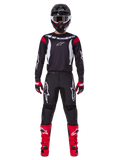 Alpinestars 2025 Fluid Haul Gear Set, Motocross rider in full racing gear, black jersey with red shoulder accents and white logos, black pants with white star branding, bright red boots, red and black gloves, black helmet with white goggles, coordinated off-road performance look