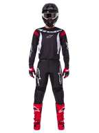 Alpinestars 2025 Fluid Haul Gear Set, Motocross rider in full racing gear, black jersey with red shoulder accents and white logos, black pants with white star branding, bright red boots, red and black gloves, black helmet with white goggles, coordinated off-road performance look