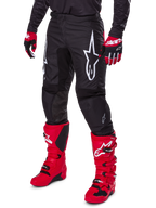 Alpinestars 2025 Fluid Haul Pants, Motocross Pants, Black, featuring a large white Alpinestars logo, worn with bright red boots and red and black gloves, durable 600D polyfabric construction with ergonomic cut for off-road racing