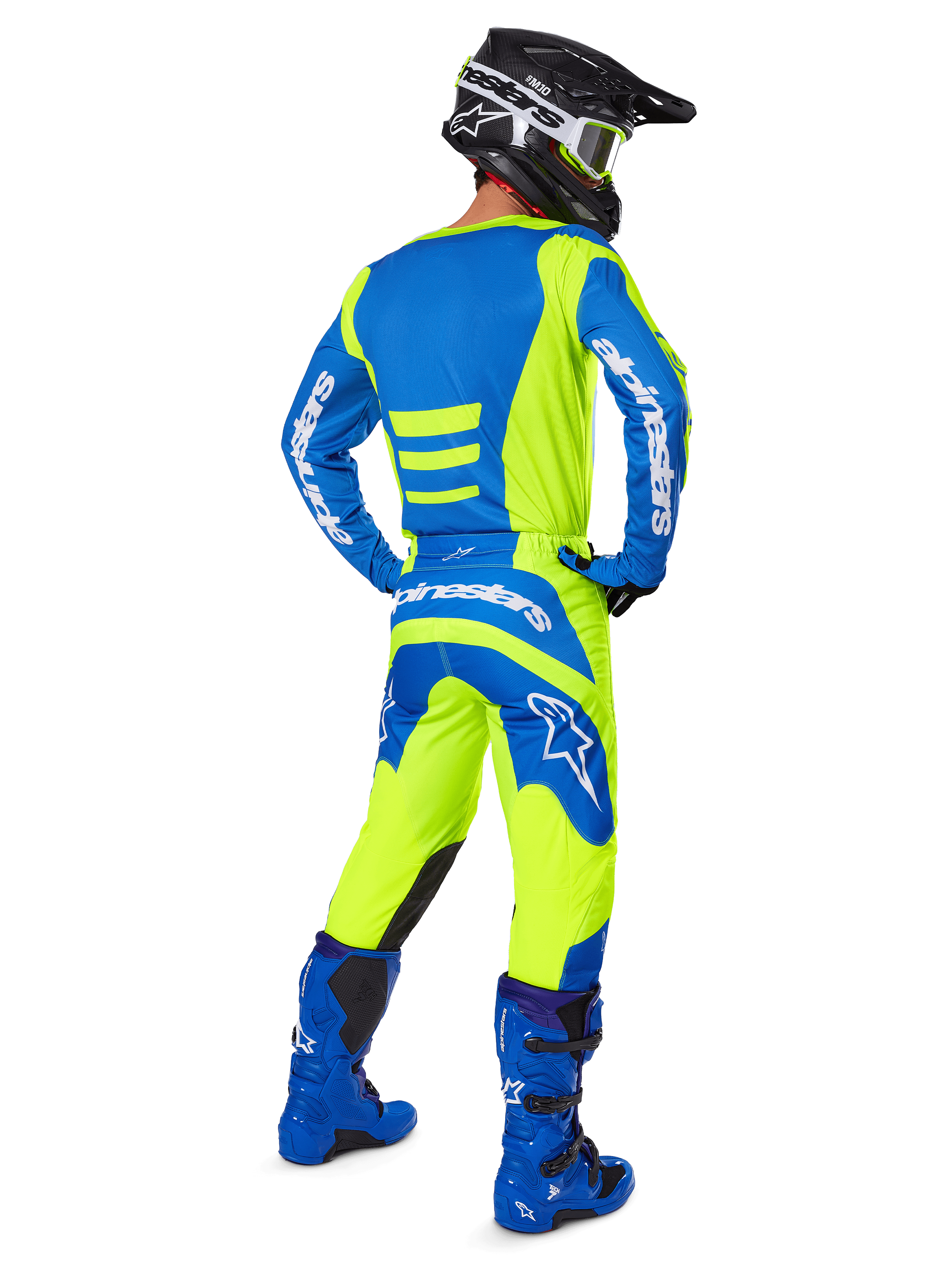Piloto de motocross visto desde atrás vistiendo los pantalones Alpinestars 2025 Fluid Haul y el jersey a juego en amarillo flúor y azul, coordinado con botas azules y un casco Alpinestars negro, equipamiento profesional de carreras todoterreno