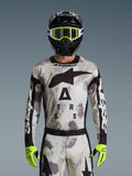 Piloto de motocross con el jersey Alpinestars Racer Lahnd 2026, patrón Sand Camo en gris y blanco, logotipo Astar grande en negro y marca en el pecho, combinado con un casco negro, gafas y guantes amarillo neón, equipamiento de alto rendimiento para conducción off-road