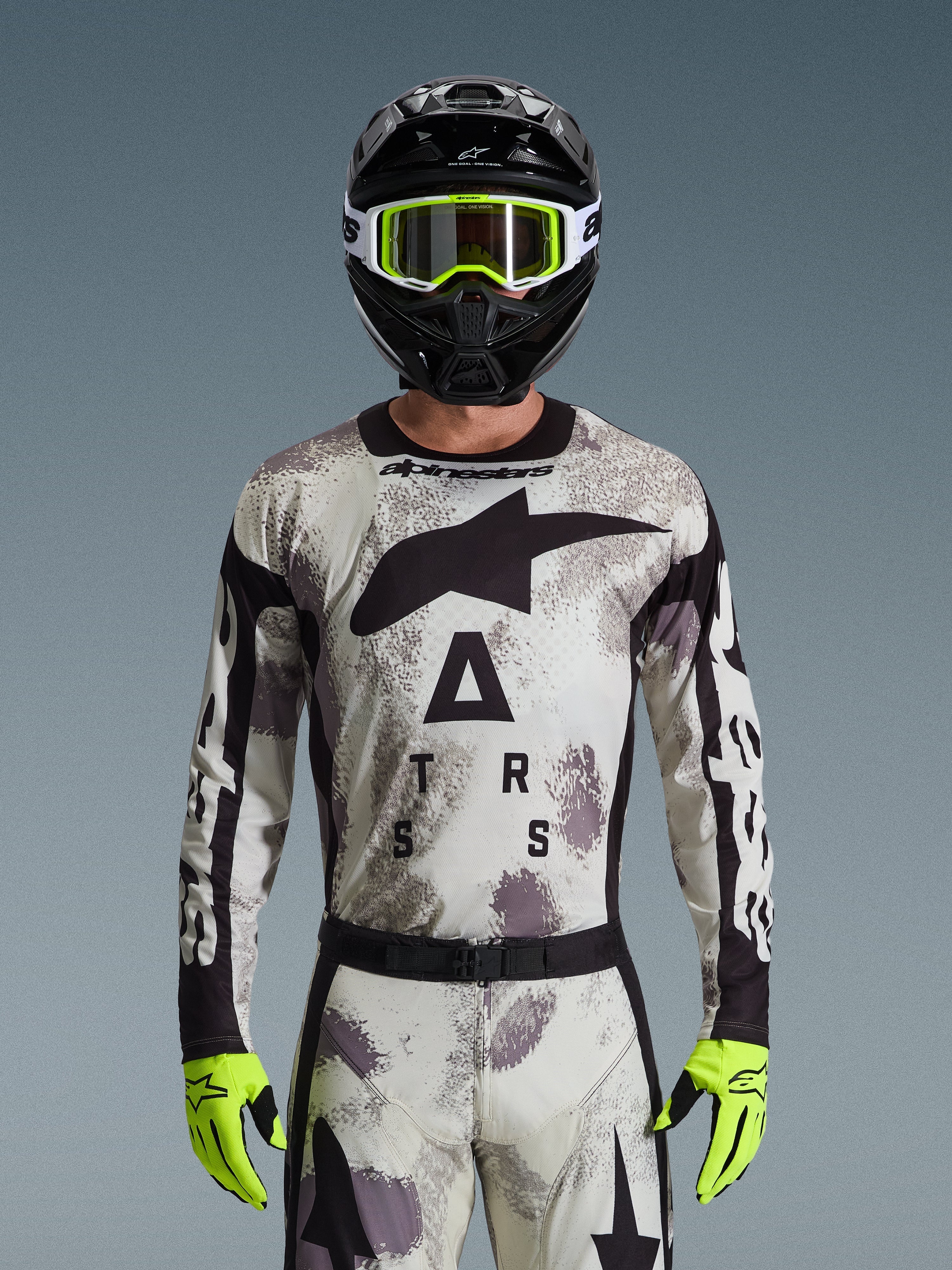 Piloto de motocross con el jersey Alpinestars Racer Lahnd 2026, patrón Sand Camo en gris y blanco, logotipo Astar grande en negro y marca en el pecho, combinado con un casco negro, gafas y guantes amarillo neón, equipamiento de alto rendimiento para conducción off-road
